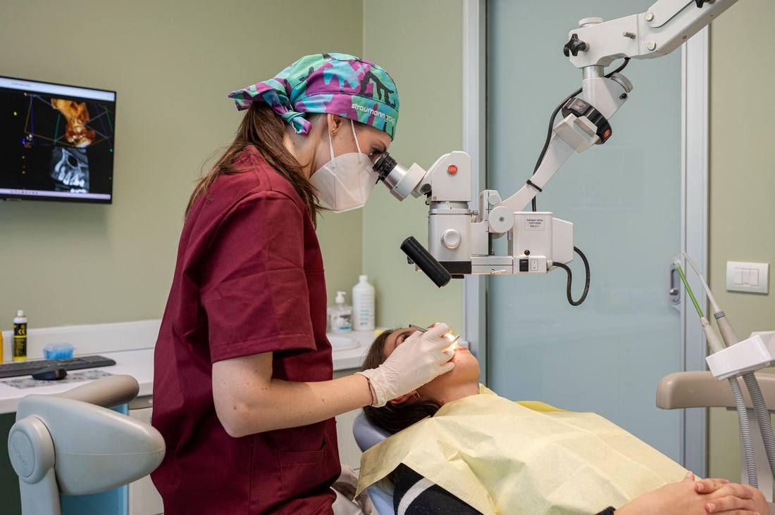 Un'odontoiatra al microscopio operatorio durante un trattamento